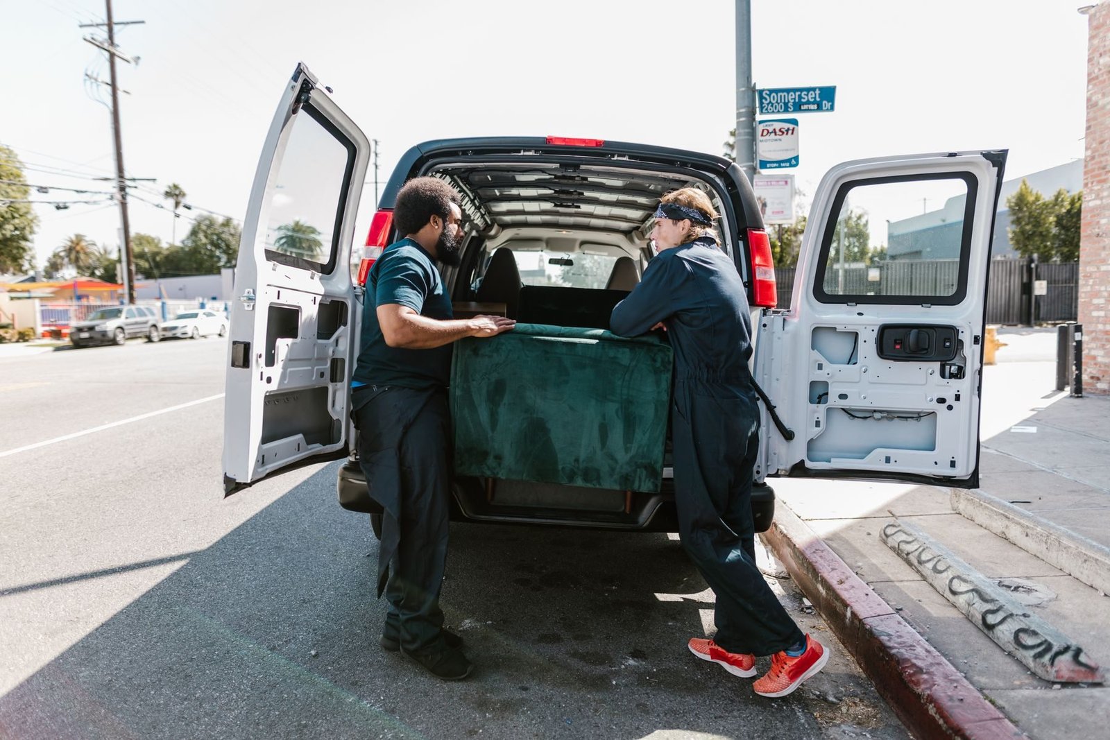 Two uniformed workers loading a sofa into a white cargo van