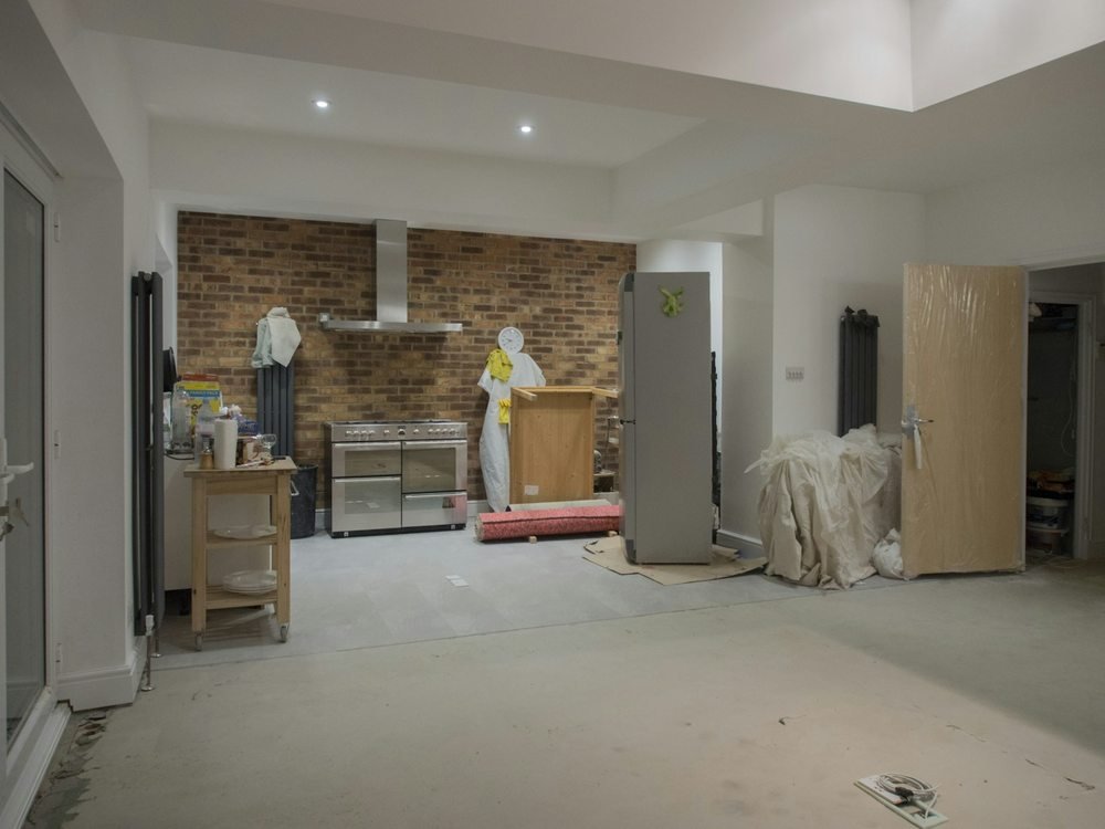 Unfinished kitchen with exposed brick, appliances and removed finishes