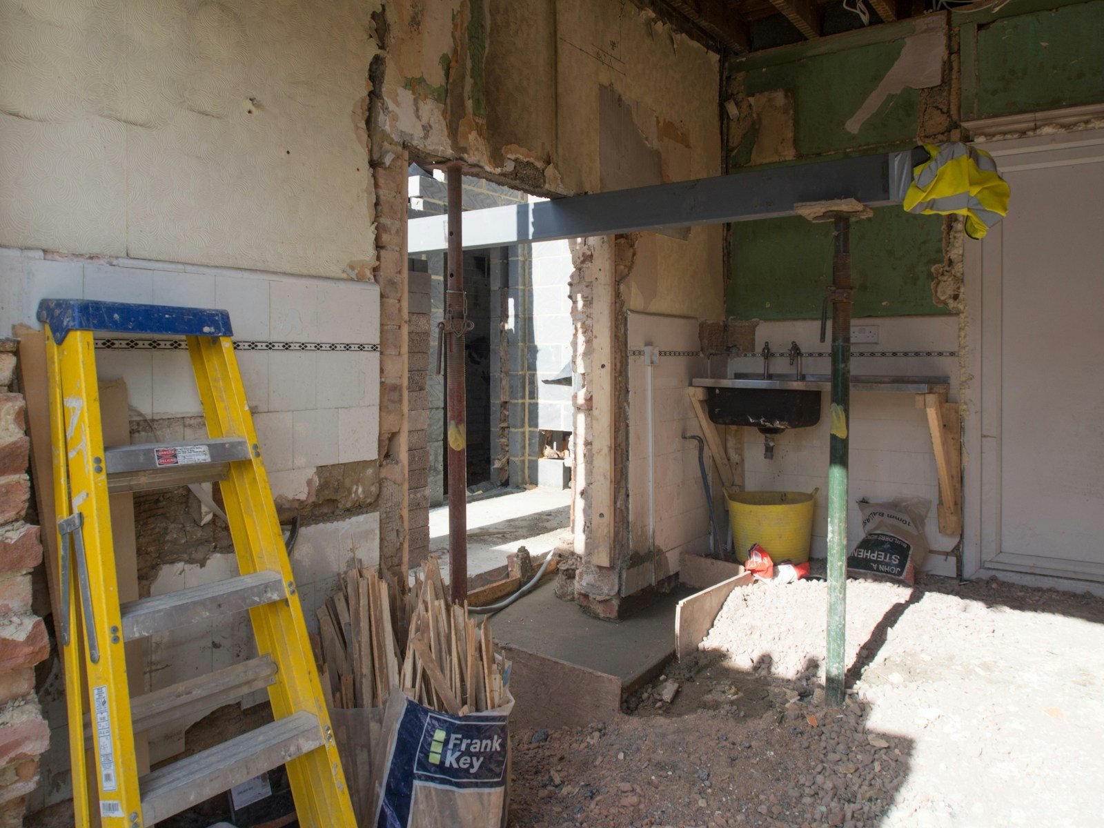 Kitchen interior stripped back during demolition, with a ladder and rubble